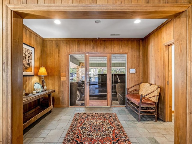 entryway with stone tile floors, wooden walls, visible vents, and crown molding