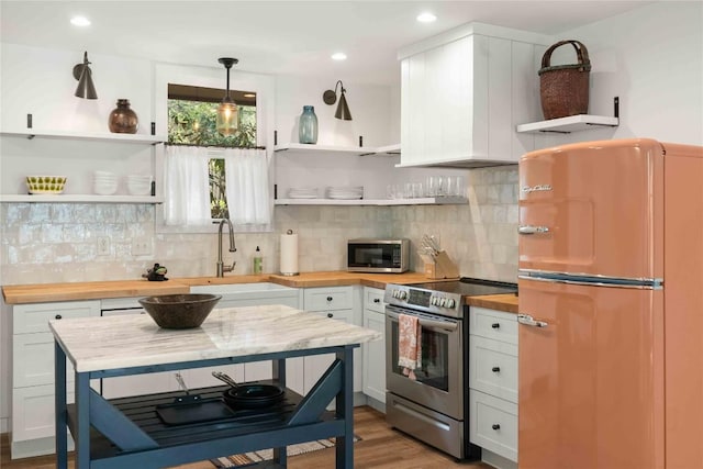 kitchen featuring wooden counters, open shelves, wood finished floors, a sink, and stainless steel appliances