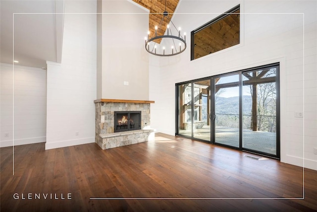 unfurnished living room featuring a stone fireplace, hardwood / wood-style flooring, high vaulted ceiling, baseboards, and a notable chandelier