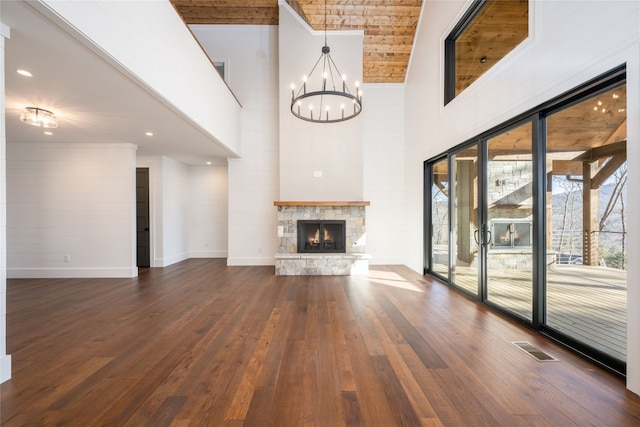 unfurnished living room featuring a high ceiling, a stone fireplace, an inviting chandelier, and dark hardwood / wood-style flooring