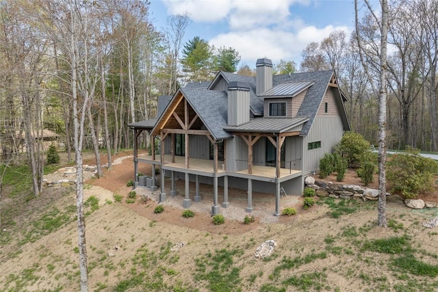 back of house featuring a standing seam roof, roof with shingles, a chimney, and metal roof