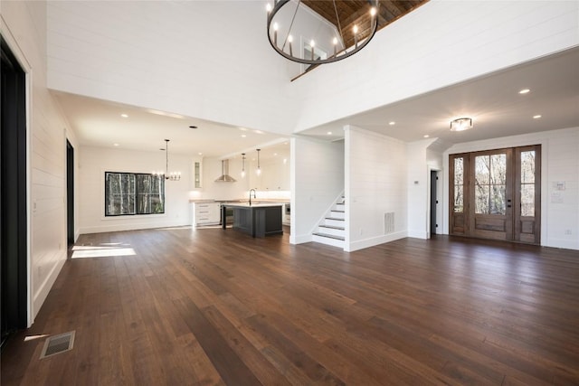 unfurnished living room with a towering ceiling, sink, dark hardwood / wood-style flooring, a chandelier, and french doors