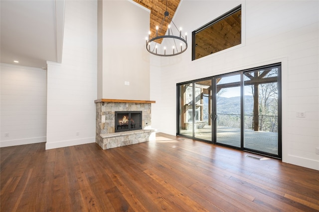 unfurnished living room featuring an inviting chandelier, hardwood / wood-style flooring, a stone fireplace, and a towering ceiling