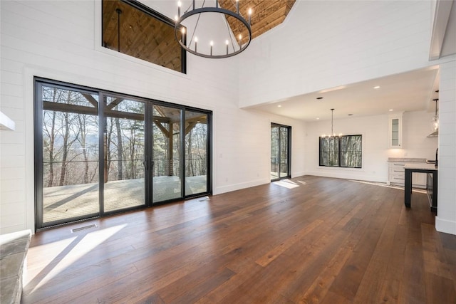 unfurnished living room with an inviting chandelier, dark wood-type flooring, and a high ceiling