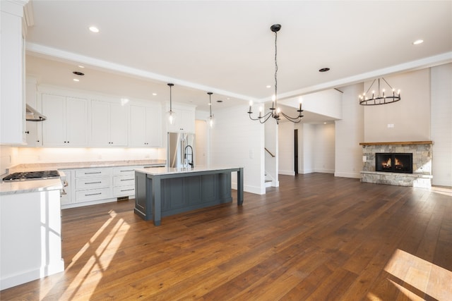 kitchen with high end fridge, white cabinetry, a center island with sink, pendant lighting, and a fireplace