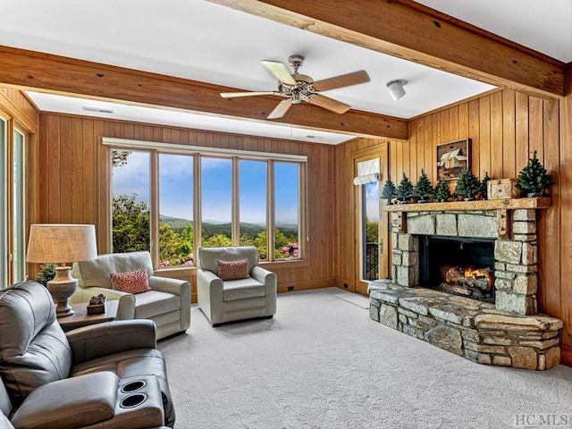 carpeted living room with beamed ceiling, plenty of natural light, a stone fireplace, and ceiling fan