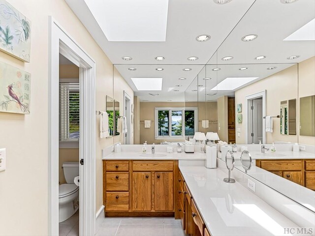 bathroom with toilet, vanity, tile patterned floors, and a skylight