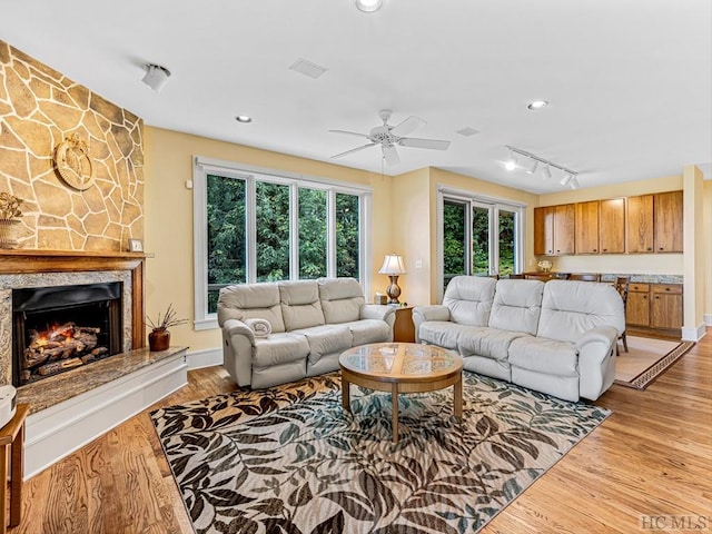 living room with a stone fireplace, light hardwood / wood-style floors, and rail lighting