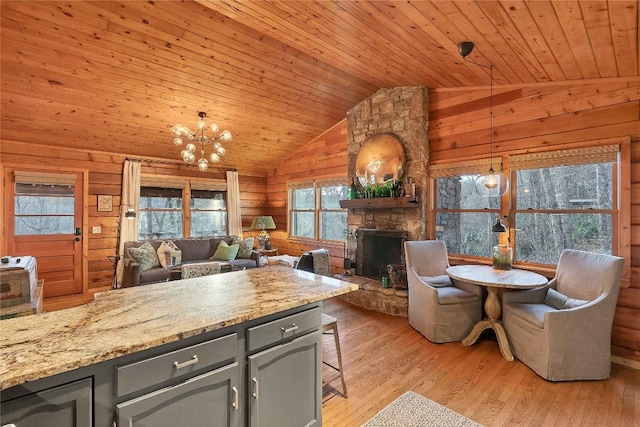 kitchen featuring wooden walls, lofted ceiling, wooden ceiling, a stone fireplace, and light wood-style floors