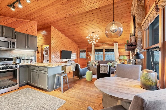 kitchen with gas range oven, stacked washer / drying machine, stainless steel microwave, wood ceiling, and open floor plan