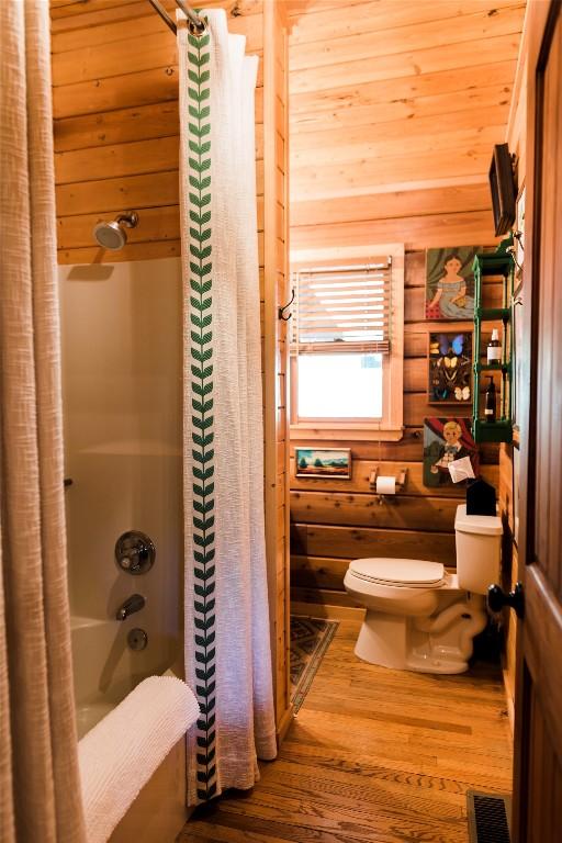 full bathroom with wooden walls, visible vents, toilet, wood finished floors, and shower / bath combo with shower curtain