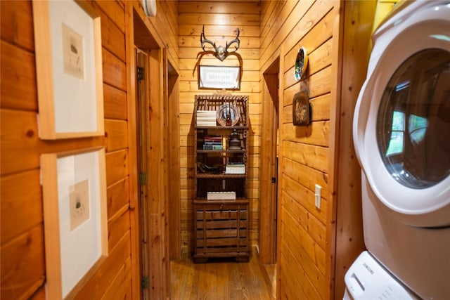 laundry room with stacked washing machine and dryer, wooden walls, and wood finished floors