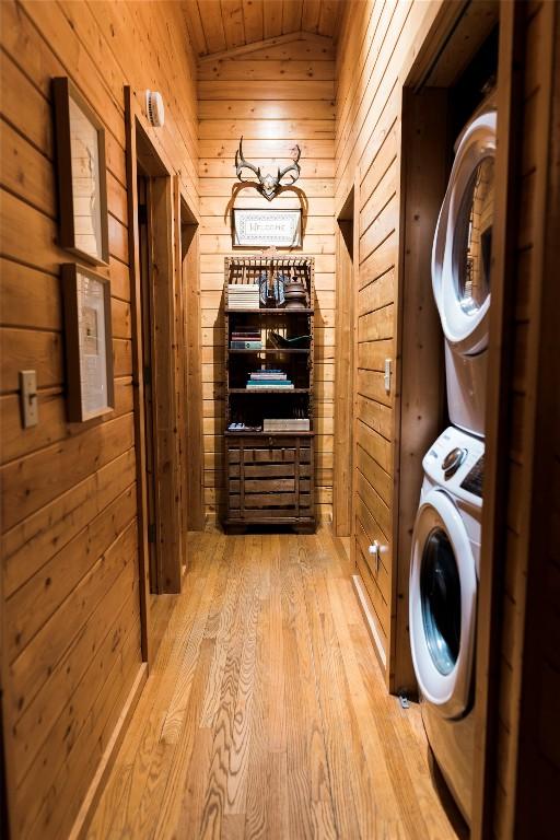 laundry area featuring laundry area, stacked washer / dryer, wood finished floors, and wooden walls