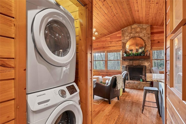 laundry room featuring wooden ceiling, wooden walls, stacked washer and dryer, a fireplace, and light wood-type flooring