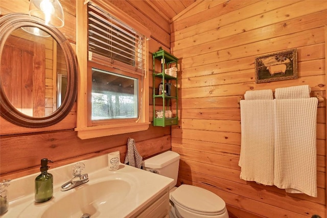 bathroom with wood walls, toilet, and vanity