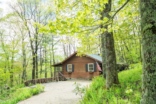 view of property exterior with crawl space, driveway, log siding, and a wooded view
