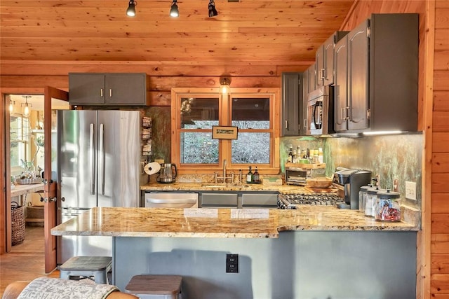 kitchen with wooden ceiling, appliances with stainless steel finishes, a peninsula, light stone countertops, and a kitchen bar