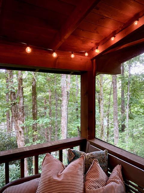 sunroom / solarium featuring beamed ceiling, a wooded view, and wood ceiling