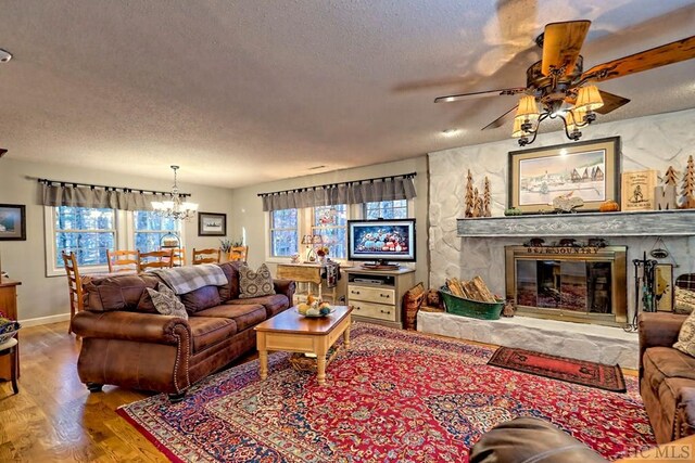 living room featuring wood-type flooring, ceiling fan with notable chandelier, a textured ceiling, and a fireplace