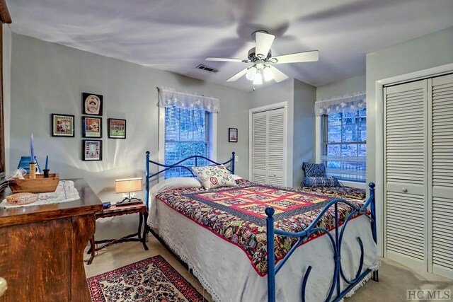 bedroom with two closets, light colored carpet, and ceiling fan