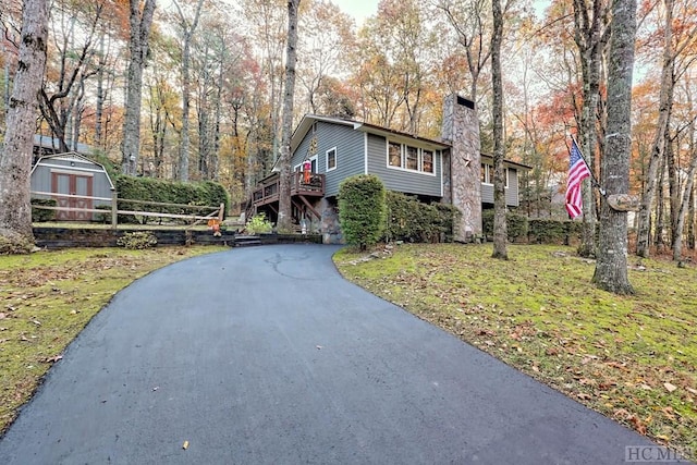 front facade with a deck, a front lawn, and a storage shed