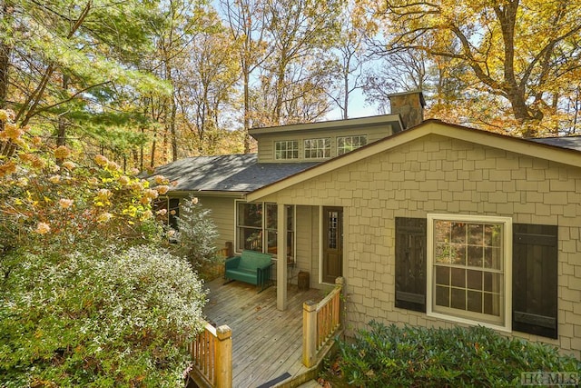 rear view of property with a deck, a shingled roof, and a chimney