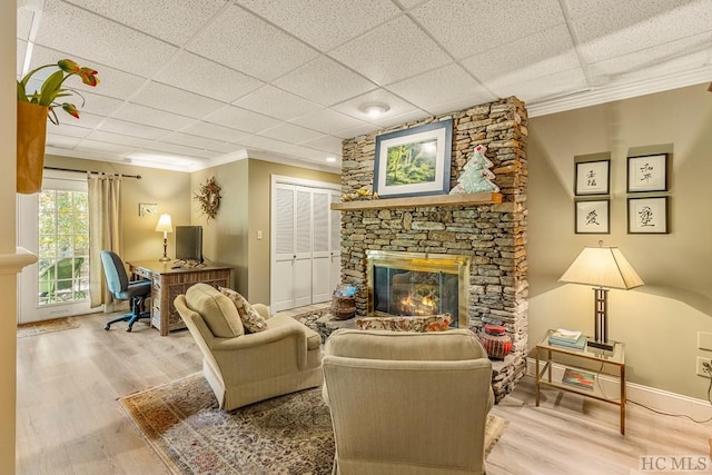 living room featuring a stone fireplace, a paneled ceiling, wood finished floors, baseboards, and crown molding