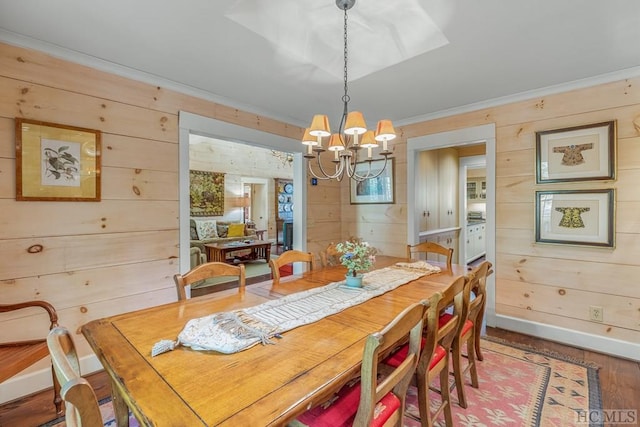 dining space featuring baseboards, ornamental molding, wood finished floors, wood walls, and a chandelier