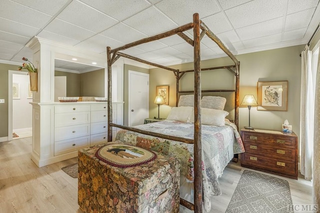 bedroom featuring light wood-style floors, a paneled ceiling, crown molding, and baseboards