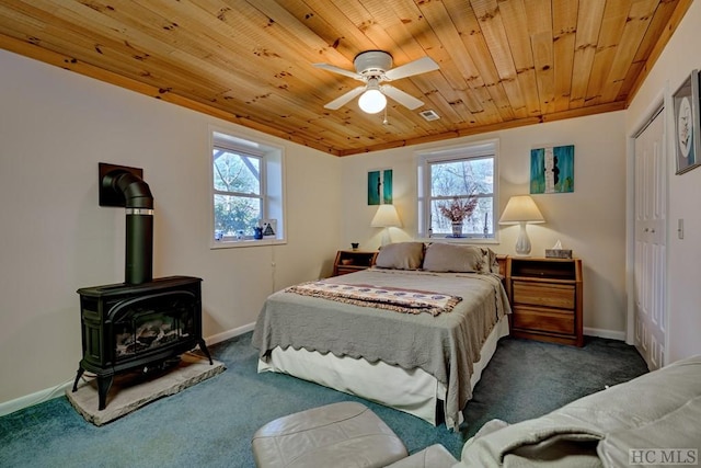 carpeted bedroom featuring ceiling fan, a wood stove, multiple windows, and wooden ceiling