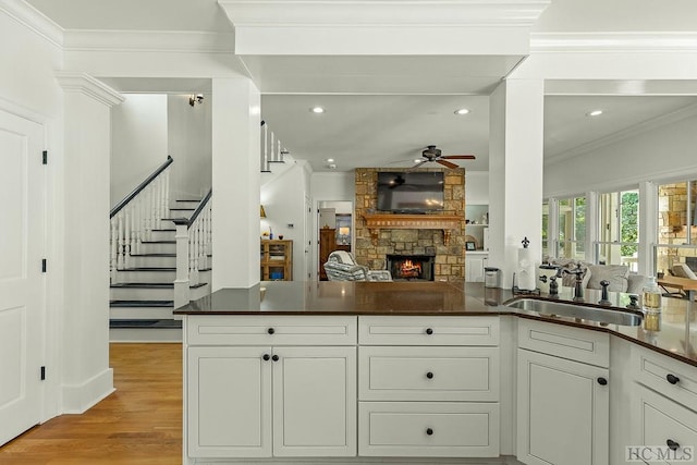 kitchen with sink, kitchen peninsula, ceiling fan, a fireplace, and white cabinets