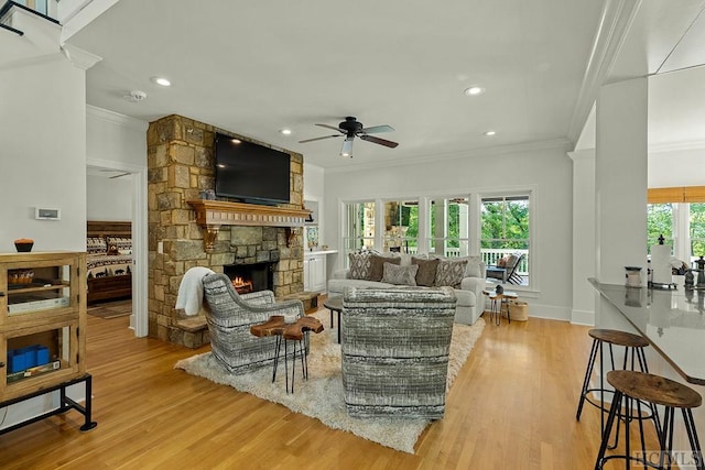 living room with a stone fireplace, crown molding, light hardwood / wood-style flooring, plenty of natural light, and ceiling fan