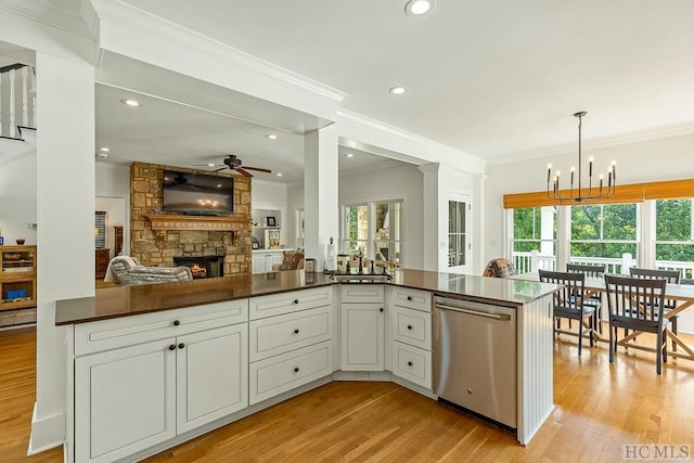 kitchen with ceiling fan with notable chandelier, dishwasher, white cabinetry, hanging light fixtures, and a stone fireplace