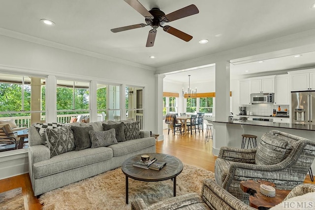 living room featuring crown molding, light hardwood / wood-style flooring, and ceiling fan with notable chandelier