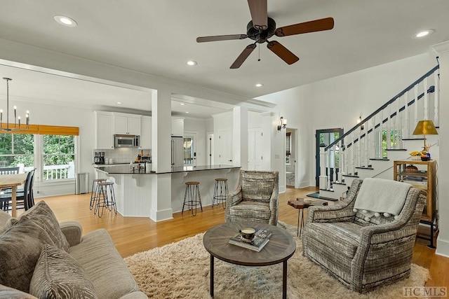 living room with ceiling fan with notable chandelier and light hardwood / wood-style flooring