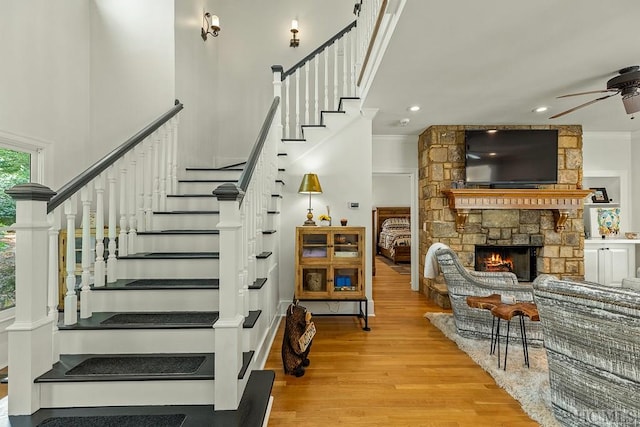 staircase with crown molding, a stone fireplace, wood-type flooring, and ceiling fan