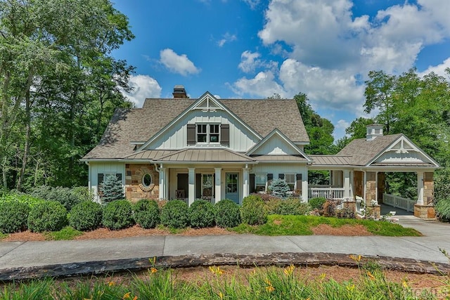 view of front of home featuring a standing seam roof, board and batten siding, covered porch, metal roof, and a chimney