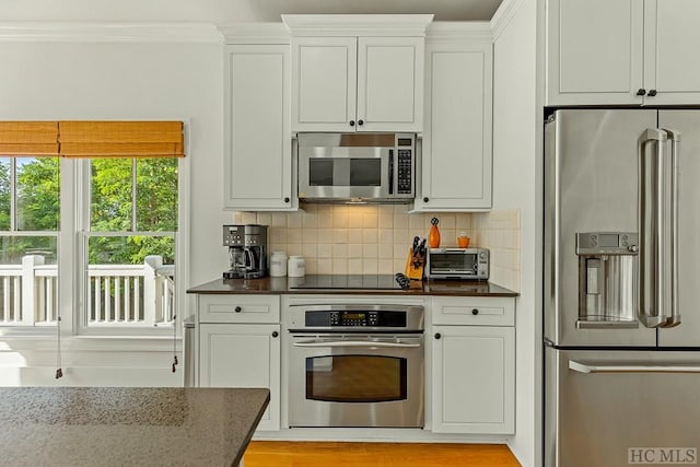 kitchen with crown molding, dark stone countertops, backsplash, stainless steel appliances, and white cabinets