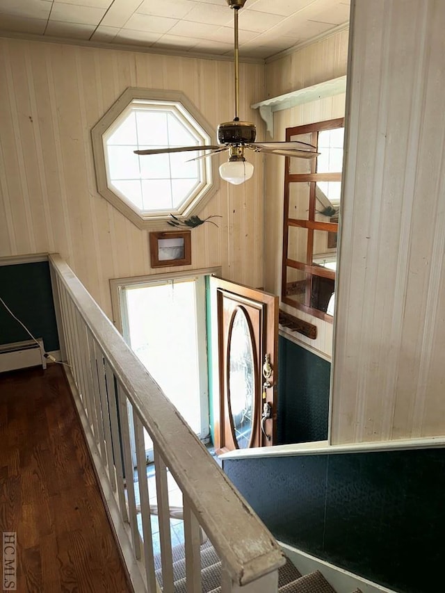 stairway featuring ceiling fan, a baseboard radiator, hardwood / wood-style floors, and wood walls