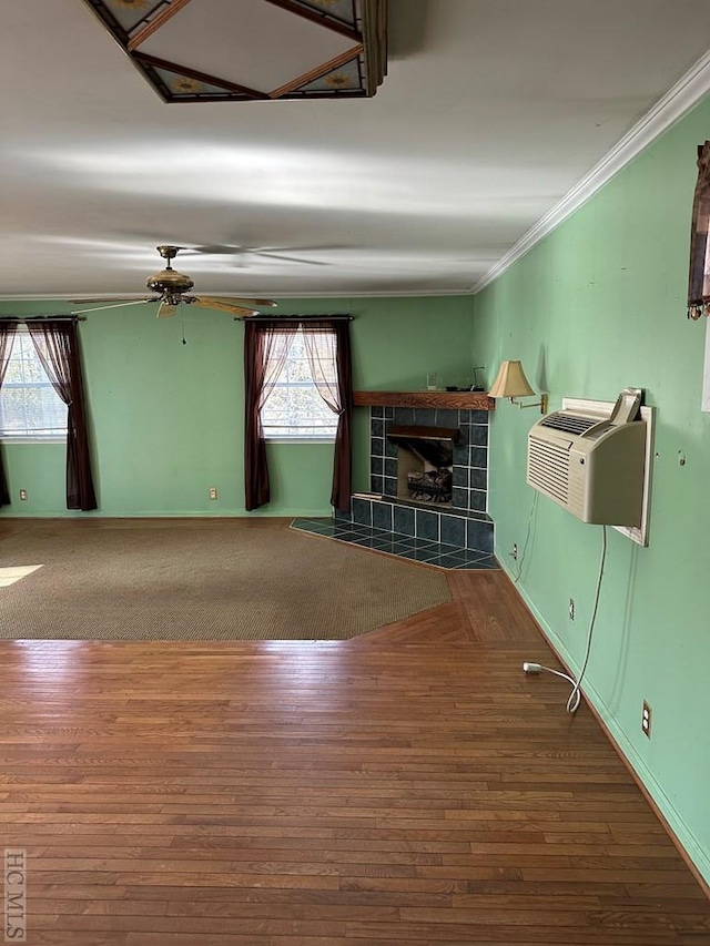 interior space with ornamental molding, a tiled fireplace, wood-type flooring, and a wall unit AC