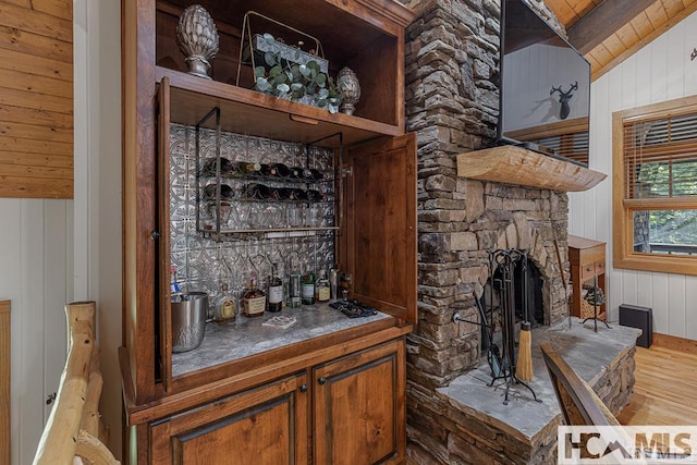 indoor dry bar featuring wood finished floors, wood walls, a stone fireplace, and wooden ceiling