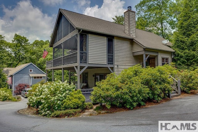 view of front of house with a chimney, an outbuilding, a sunroom, a shingled roof, and a porch