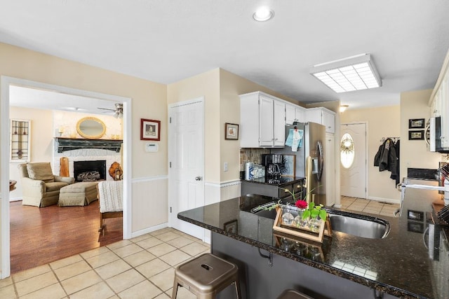 150 Lauren Ln, Franklin, NC 28734 - kitchen featuring light tile patterned floors, white cabinets, stainless steel appliances, a stone fireplace, and wainscoting