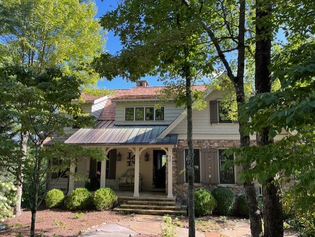 view of front of home featuring a standing seam roof, covered porch, stone siding, and metal roof