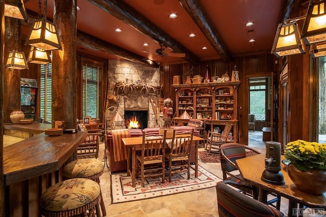 dining space with beam ceiling, a stone fireplace, and wooden walls