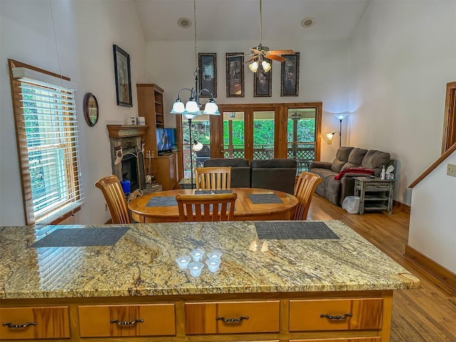 dining space featuring ceiling fan, healthy amount of natural light, wood finished floors, a fireplace with raised hearth, and high vaulted ceiling