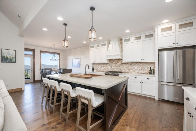 kitchen featuring dark wood-style floors, high end fridge, custom exhaust hood, and light countertops