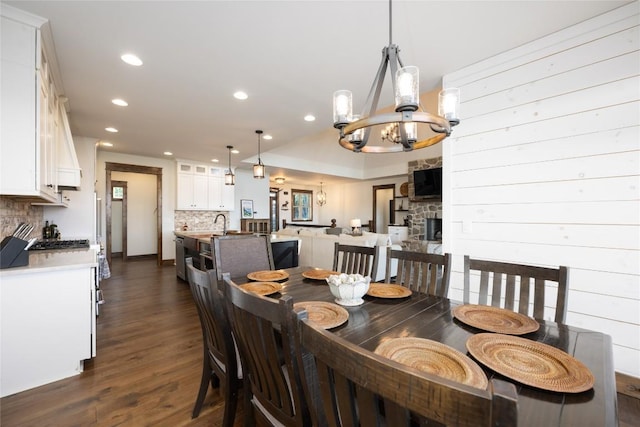 dining space with a stone fireplace, recessed lighting, a notable chandelier, dark wood-style flooring, and vaulted ceiling