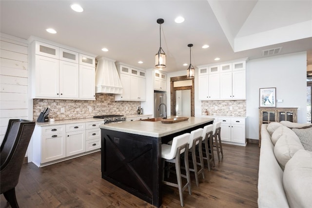 kitchen featuring a breakfast bar area, visible vents, light countertops, custom exhaust hood, and range