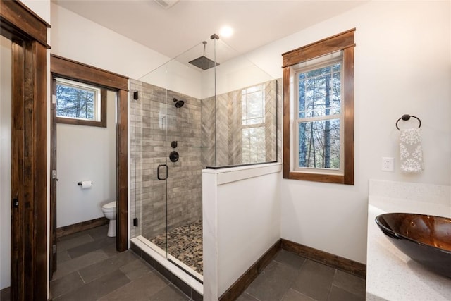 bathroom with toilet, a shower stall, baseboards, and a wealth of natural light